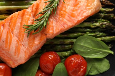 Photo of Tasty grilled salmon with tomatoes, asparagus, spinach and rosemary on plate, top view