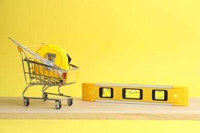 Photo of Small shopping cart and set of construction tools on yellow background