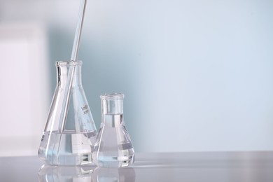 Photo of Laboratory analysis. Glass flasks and stirring rod on white table against blurred background, space for text