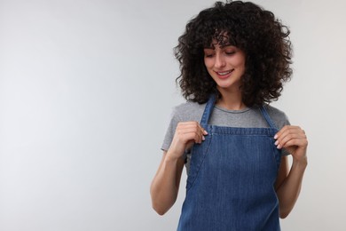 Photo of Happy woman wearing kitchen apron on light grey background, space for text. Mockup for design