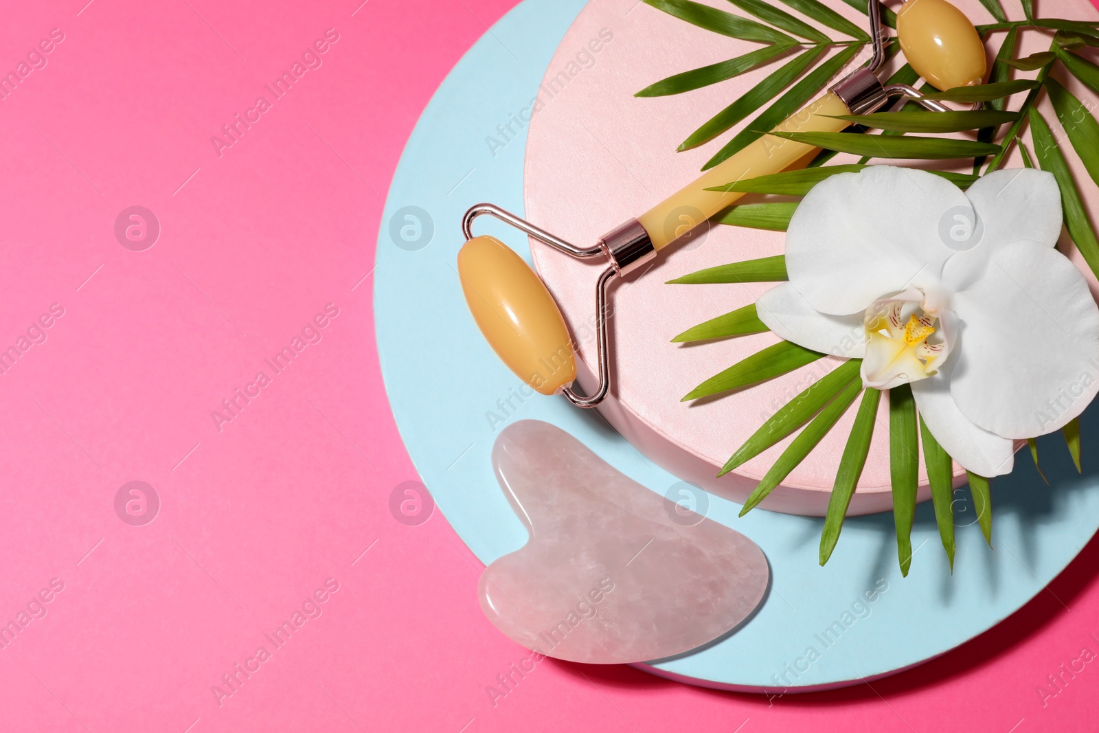 Photo of Beautiful composition with gua sha stone and face roller on pink background, top view. Space for text