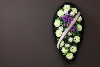 Funeral wreath of plastic flowers with ribbon hanging on dark grey wall, space for text