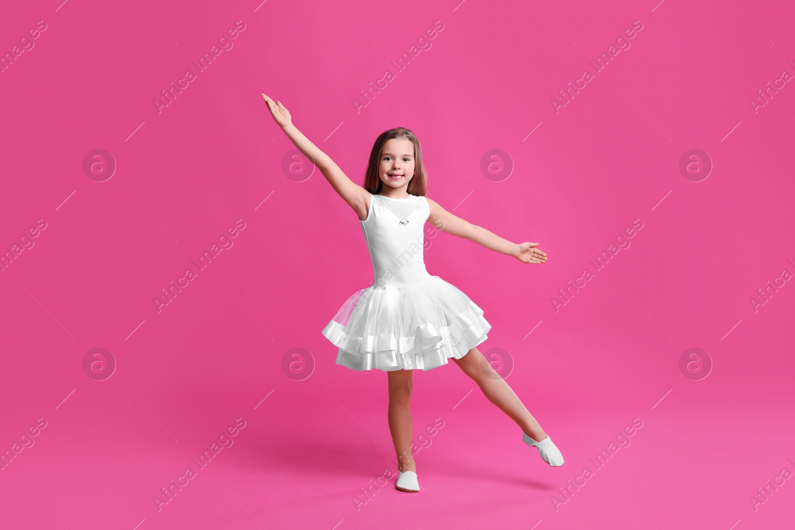Photo of Cute little girl in white dress dancing on pink background