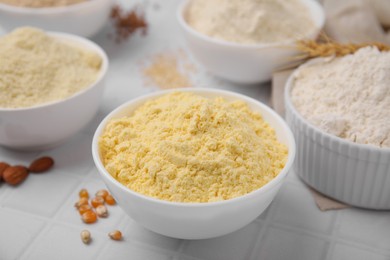 Photo of Bowls with different types of flour on tiled table, closeup