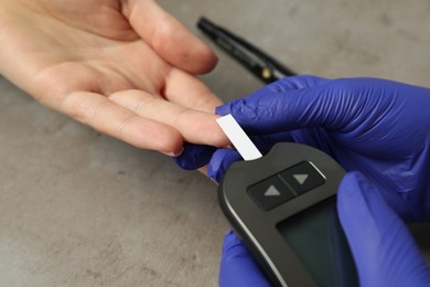 Photo of Diabetes. Doctor checking patient's blood sugar level with glucometer at gray table, closeup