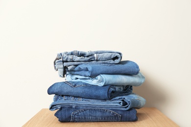 Photo of Stack of different jeans on table against light background