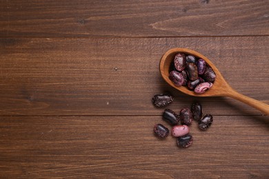 Photo of Spoon and dry kidney beans on wooden table, flat lay. Space for text