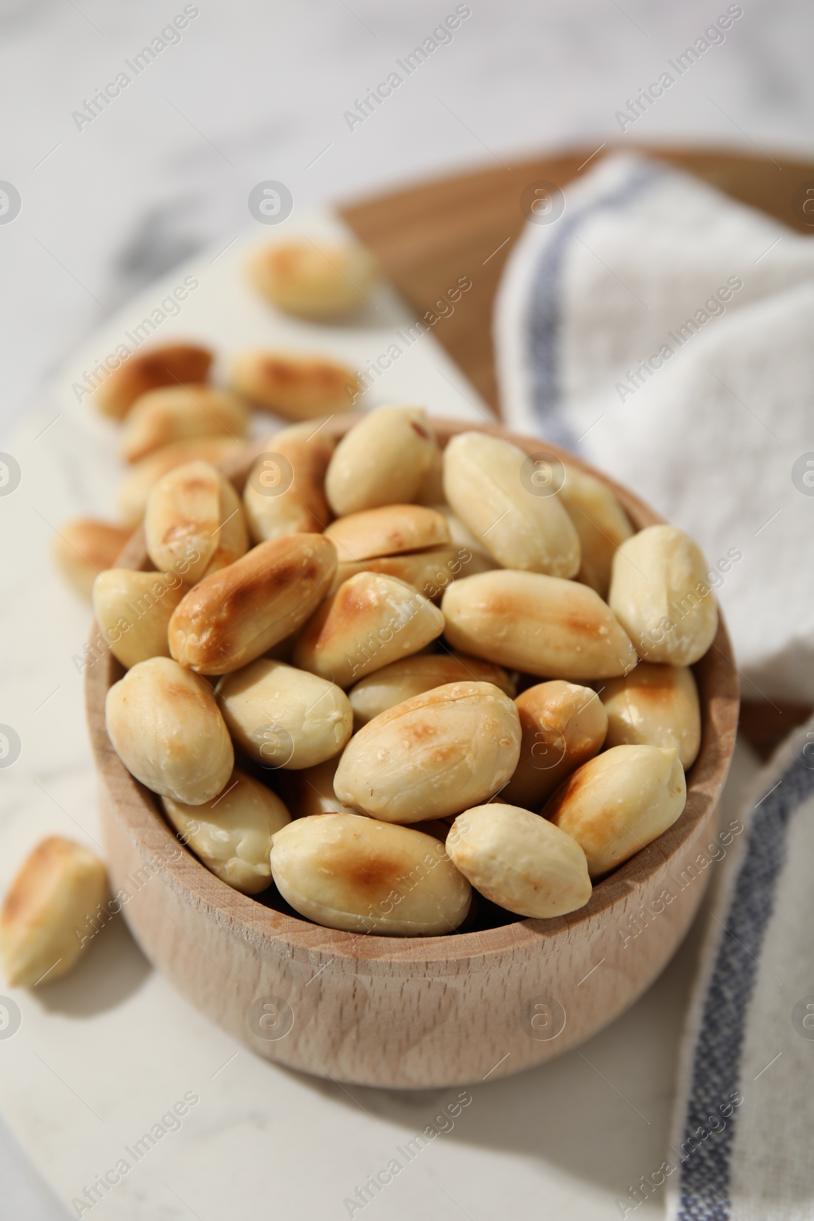 Photo of Roasted peanuts in bowl on white table, closeup