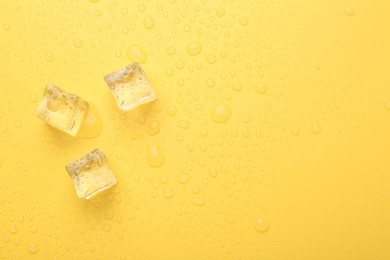 Photo of Crystal clear ice cubes on yellow background, flat lay. Space for text