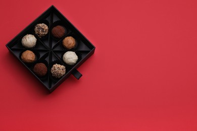 Photo of Box of tasty chocolate candies on red background, top view. Space for text