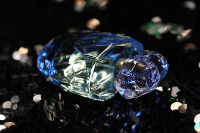 Photo of Luxury perfume in bottle on fabric with shiny sequins, closeup