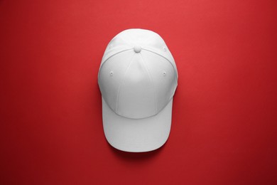 Photo of Stylish white baseball cap on red background, top view