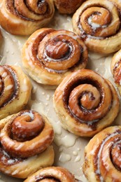 Photo of Tasty cinnamon rolls with cream on parchment paper, above view