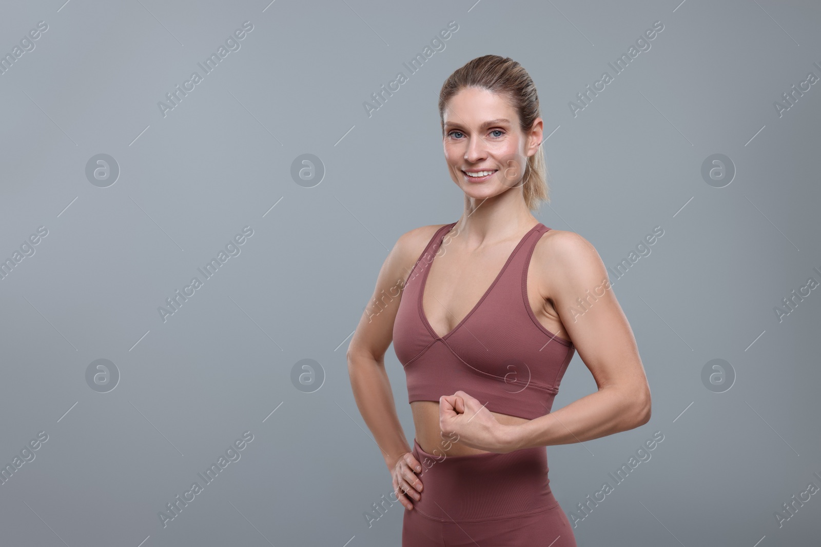 Photo of Portrait of sportswoman showing muscles on grey background, space for text