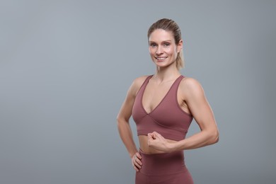 Photo of Portraitsportswoman showing muscles on grey background, space for text