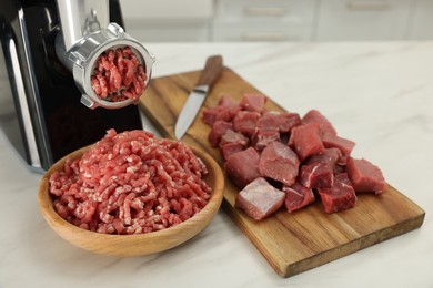 Photo of Electric meat grinder with beef on white marble table indoors