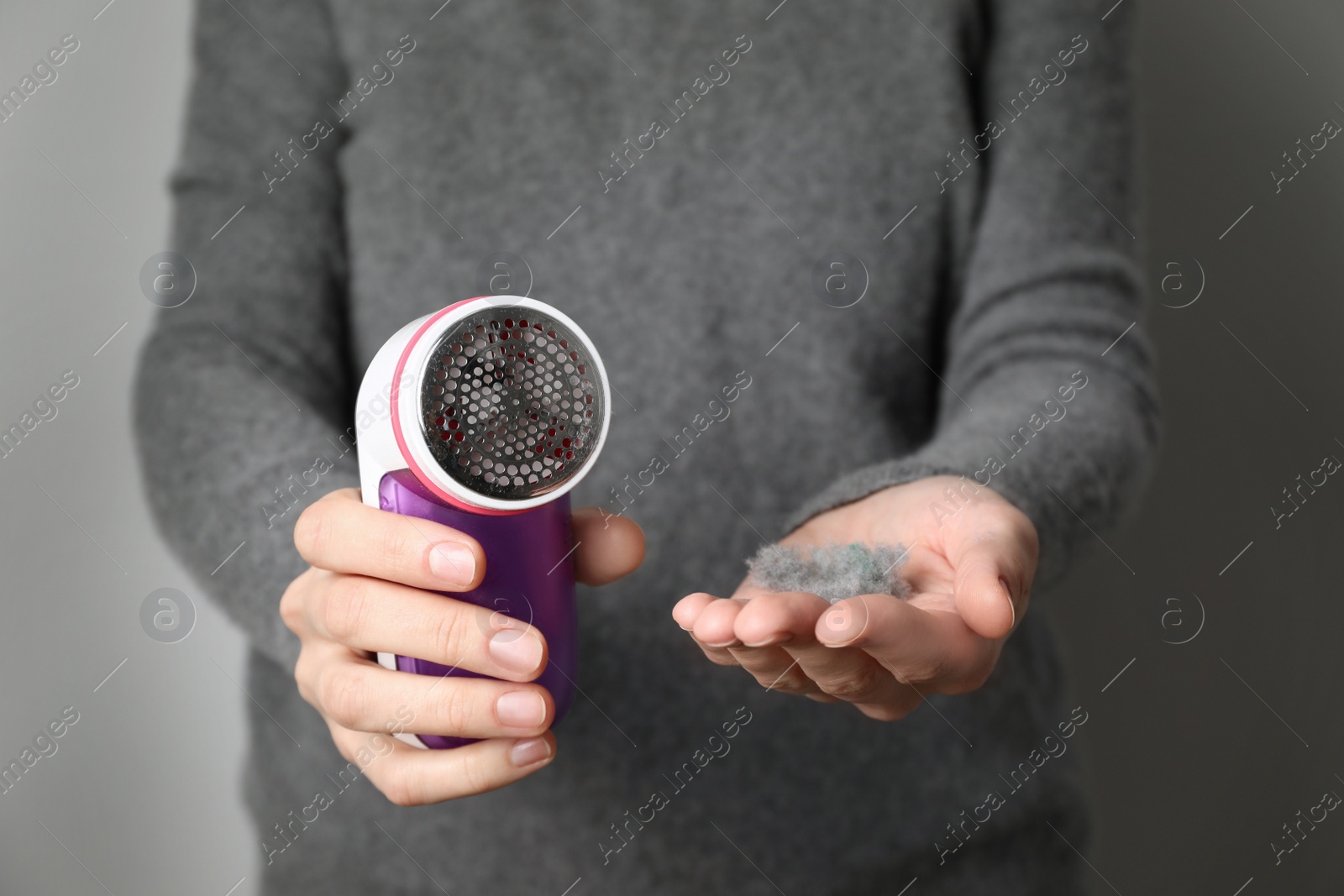 Photo of Woman in woolen sweater holding fabric shaver and lint on light grey background, closeup