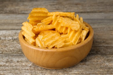 Photo of Bowl with delicious ridged potato chips on wooden table, closeup