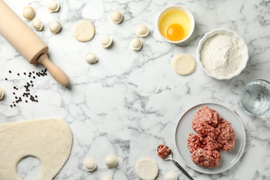 Photo of Flat lay composition with raw dumplings and ingredients on marble background, space for text. Process of cooking