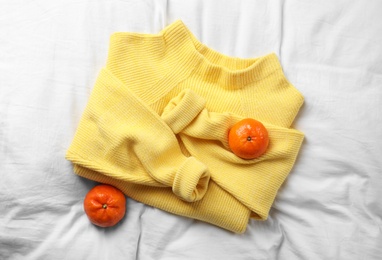 Beautiful yellow warm sweater and tangerines on white bedsheet, flat lay