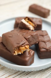 Photo of Plate of chocolate bars with caramel, nuts and nougat on white wooden table, closeup