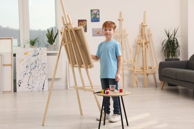 Photo of Little boy painting in studio. Using easel to hold canvas