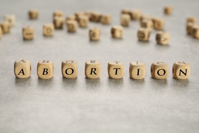 Photo of Word Abortion made of wooden cubes on grey table, closeup