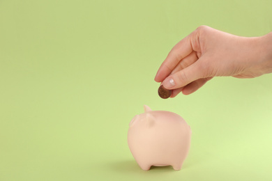 Photo of Woman putting coin into piggy bank on green background, closeup