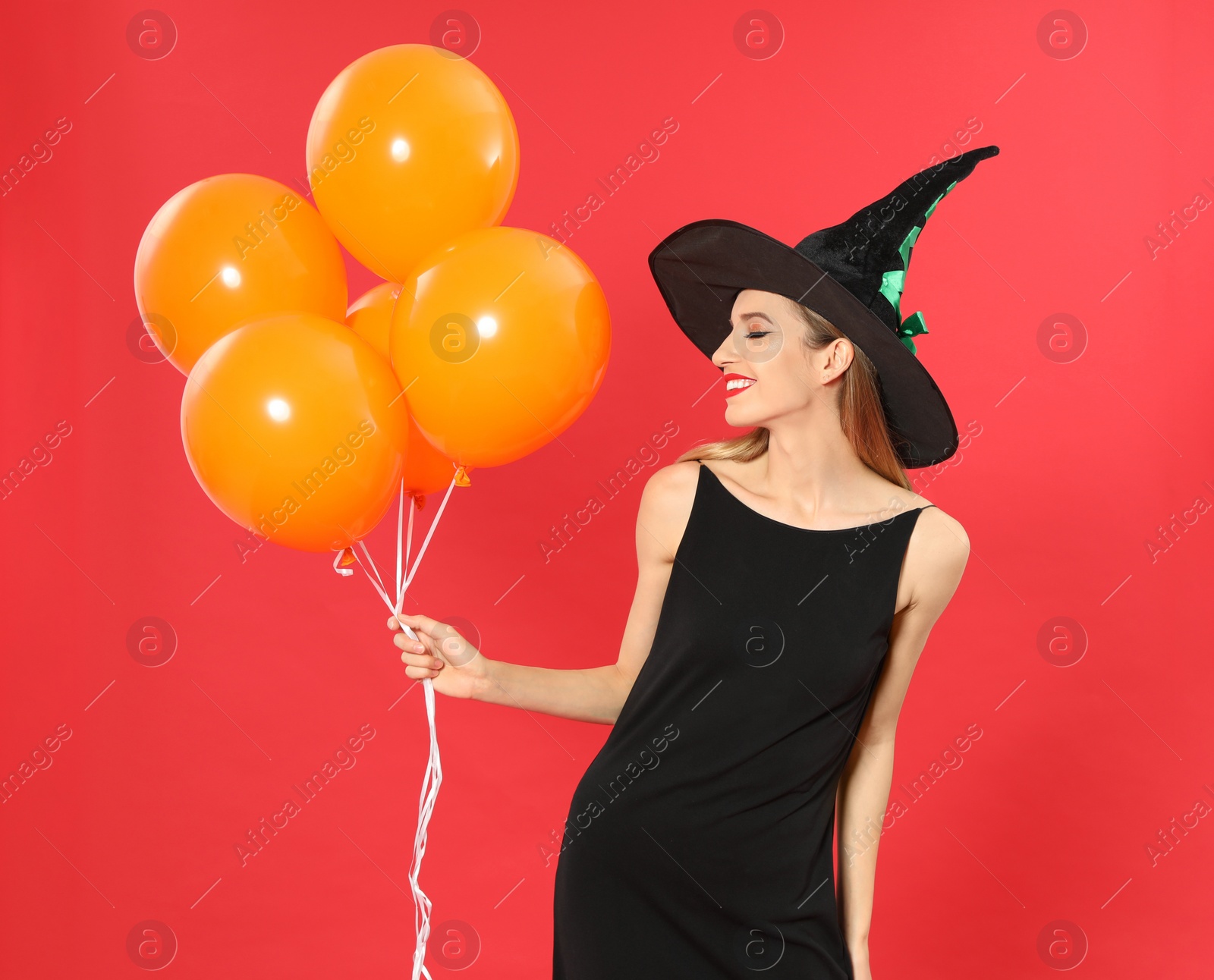 Photo of Beautiful woman wearing witch costume with balloons for Halloween party on red background