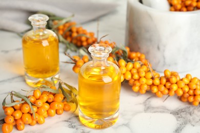 Photo of Natural sea buckthorn oil and fresh berries on white marble table