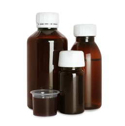 Photo of Bottles of cough syrup and measuring cup on white background