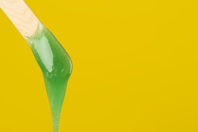 Photo of Wooden spatula with hot depilatory wax on yellow background. Space for text