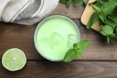 Photo of Delicious mint liqueur with green leaves and ice cubes on wooden table, flat lay