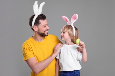 Photo of Father and son in bunny ears headbands having fun on grey background. Easter celebration