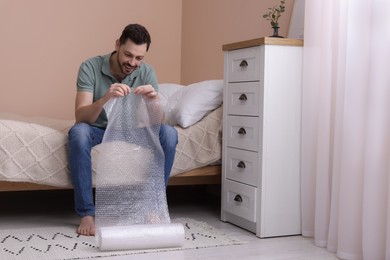 Photo of Man popping bubble wrap in bedroom at home. Stress relief