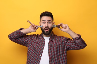 Photo of Handsome young man with mustache holding blade and shaving brush on yellow background