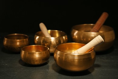 Photo of Golden singing bowls with mallets on black table against dark background