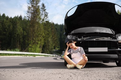 Stressed woman sitting on asphalt road near broken car outdoors, space for text