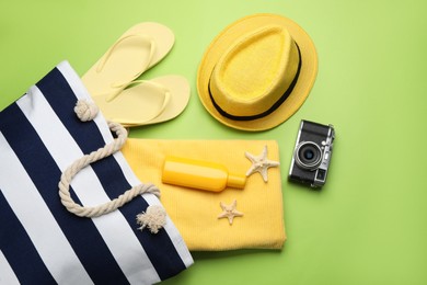 Photo of Stylish bag with beach accessories on light green background, flat lay