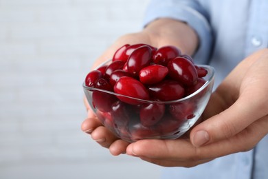 Woman with glass bowl of fresh ripe dogwood berries on light background, closeup