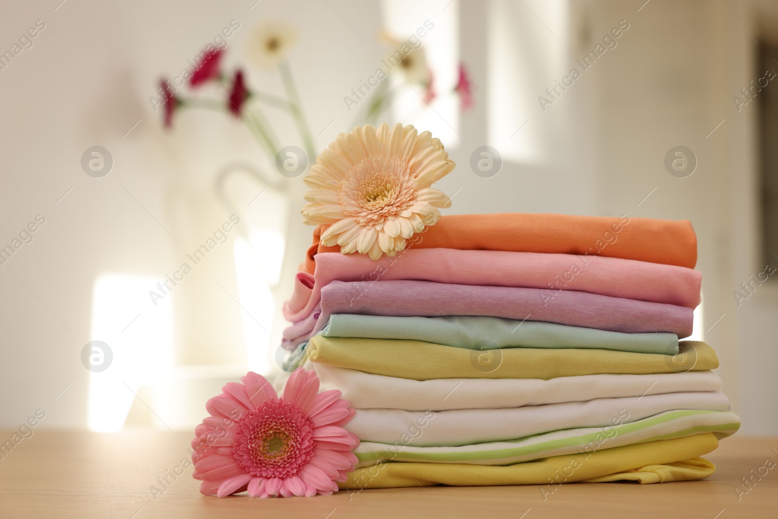 Photo of Stack of clean clothes and flowers on wooden table