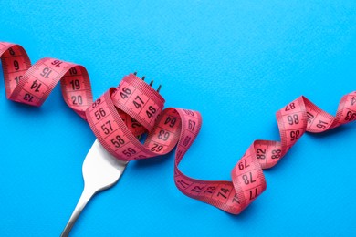 Photo of Fork with measuring tape on light blue background, top view. Diet concept