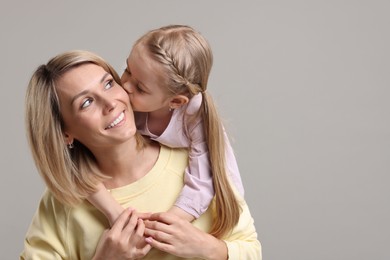 Photo of Daughter kissing her happy mother on grey background. Space for text