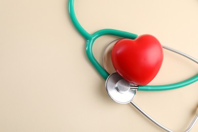 Photo of Stethoscope and red heart on beige background. Space for text
