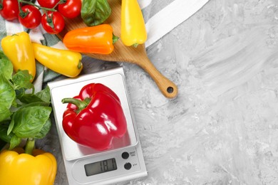 Photo of Kitchen scale with bell pepper, basil and tomatoes on grey textured table, flat lay. Space for text