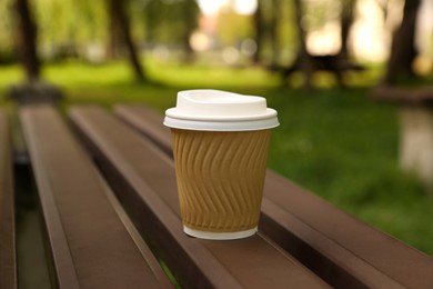 Photo of Paper cup on wooden bench in park. Coffee to go