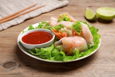 Tasty spring rolls served with lettuce and sauce on wooden table, closeup