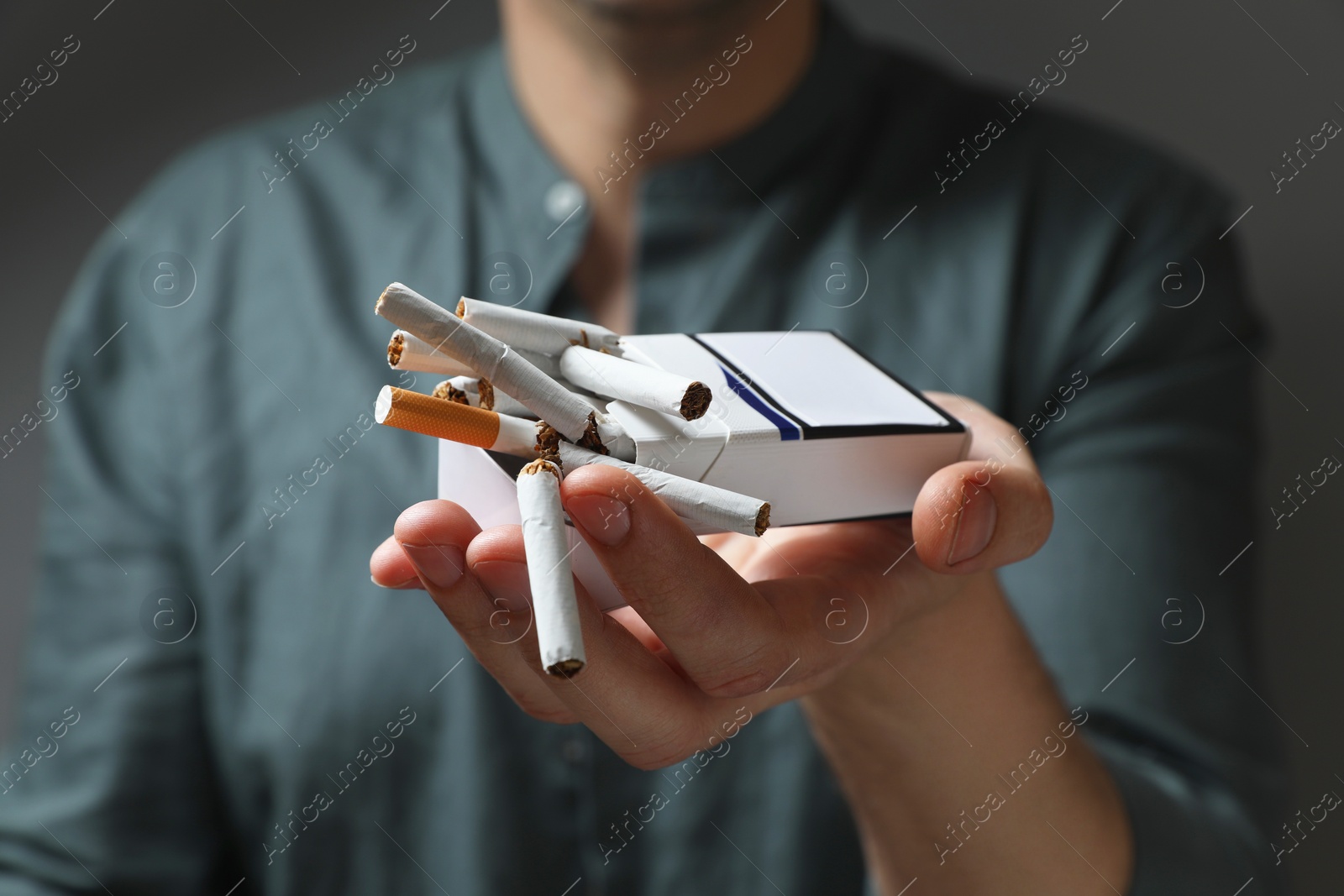 Photo of Stop smoking. Man holding pack with broken cigarettes on grey background, closeup