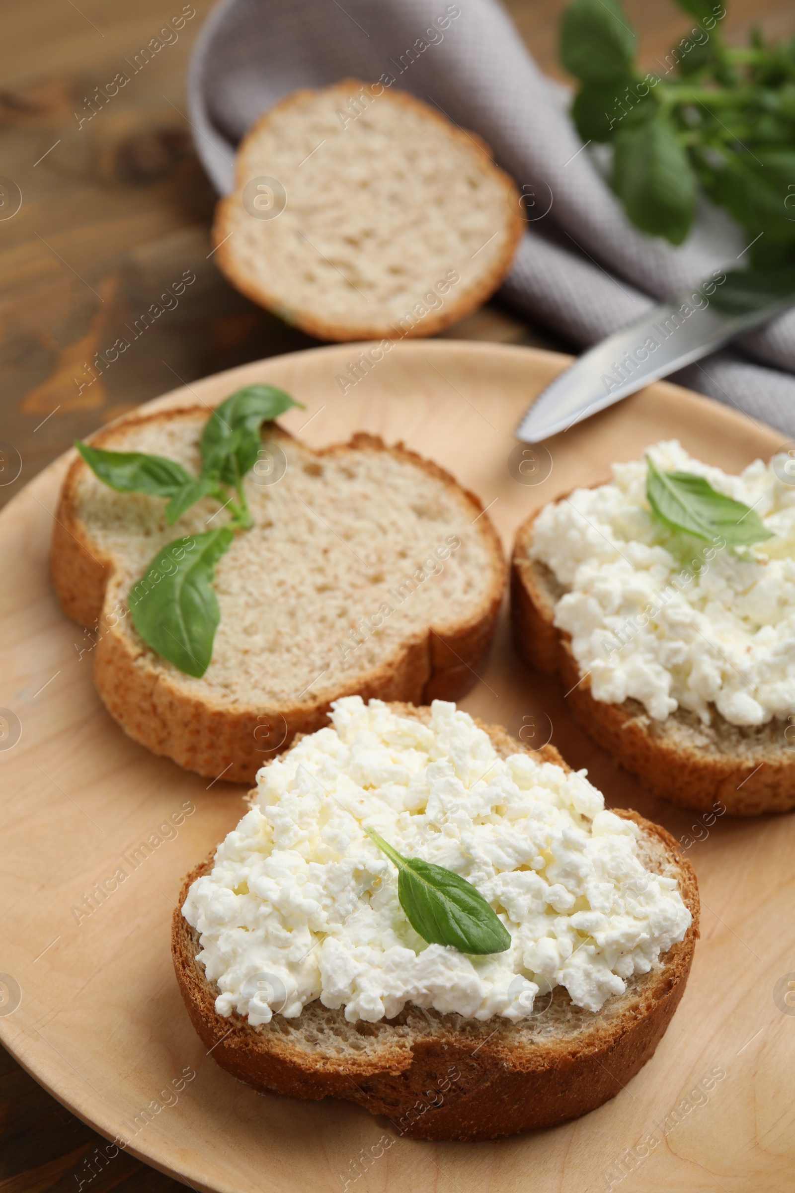 Photo of Bread with cottage cheese and basil on wooden plate, closeup