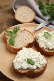 Photo of Bread with cottage cheese and basil on wooden plate, closeup